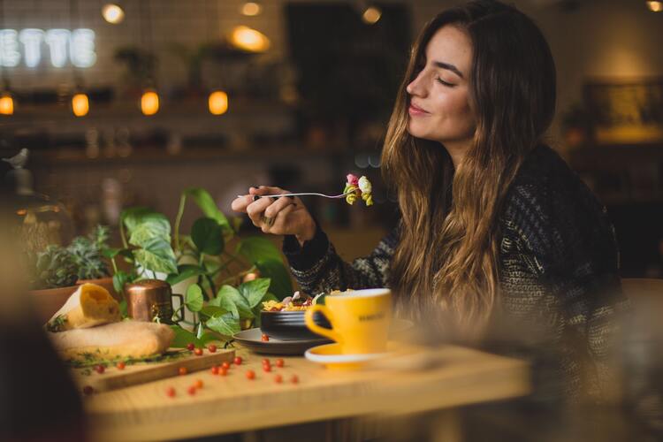 Picture of a woman sitting at a table enjoying some pasta. No Food Guilt