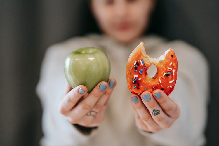 Photo of a woman choosing between a green apple and a donut with sprinkles. Healthy Eating choices or dieting.
