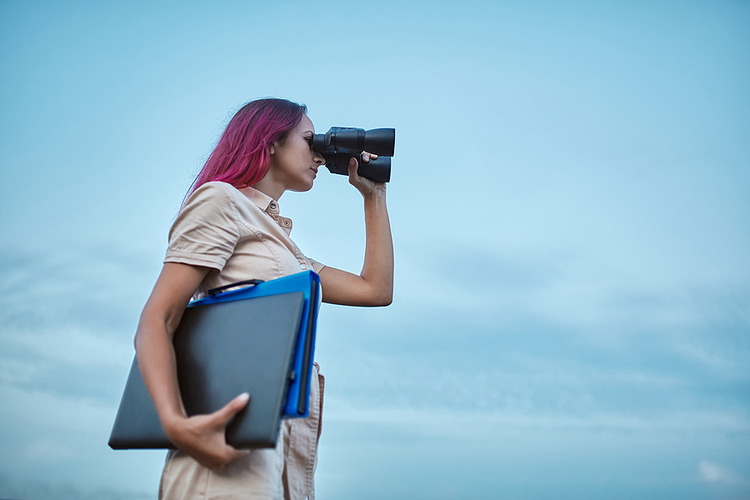 Pink-haired young Woman looking forward through binoculars holding a laptop and binder. Self-Improvement focused.