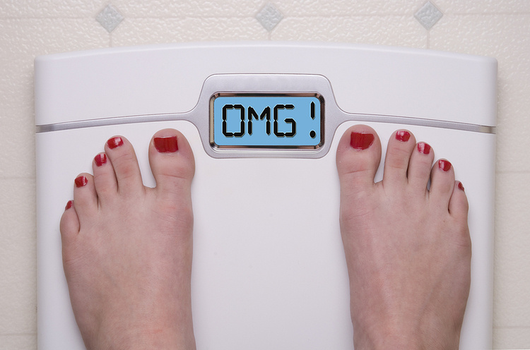 Feet on a Digital Bathroom Scale with Red Toenail Polish. The Scale Displays OMG Message. White scale with a blue screen. Hormones and Weight Gain