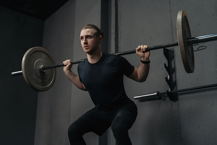 Photo of a man squatting with a barbell over his shoulders. He is fit, muscular, and dressed in all black workout clothes. Get Back into Working Out Post