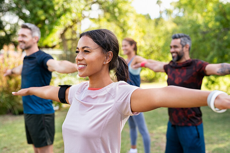 A photo of a group of people from different races standing in a field surrounded by trees. They are stretching their arms out, doing yoga exercises. Get Back into Working Out